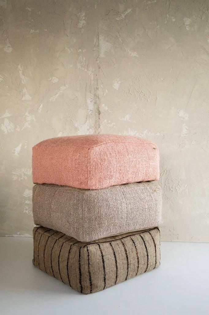 Stapel van drie katoenen poefs in roze, beige en zwart voor stijlvolle zithoek in huis of overdekte buitenruimte.