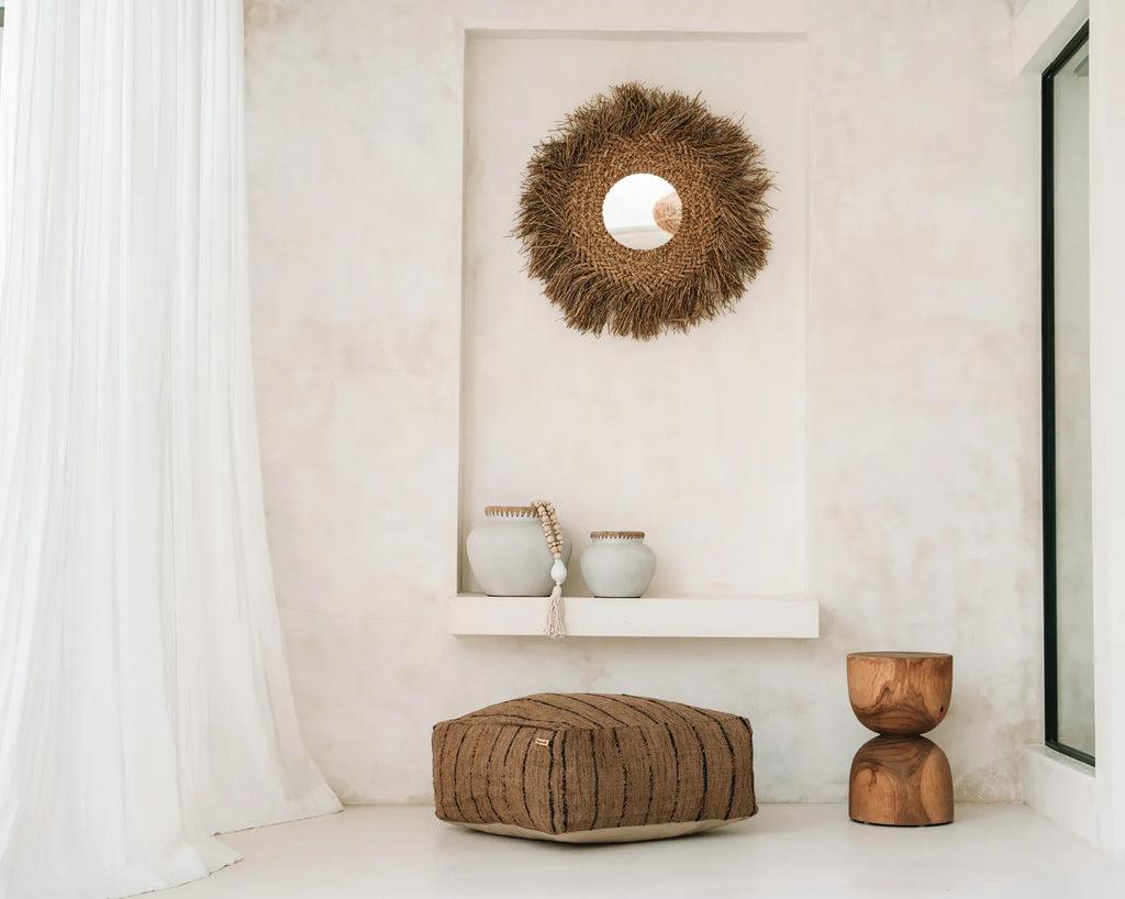 Stijlvolle katoenen poef in beige-zwart als stijlvolle woonaccessoire in moderne kamer met houten kruk en decoratieve spiegel.