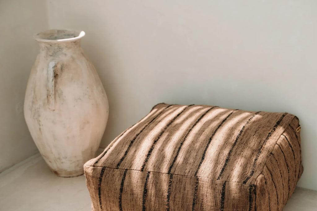 Stijlvolle beige en zwarte katoenen poef naast rustieke vaas, ideaal voor huisdecoratie en comfort. Perfect handgemaakt zitelement.