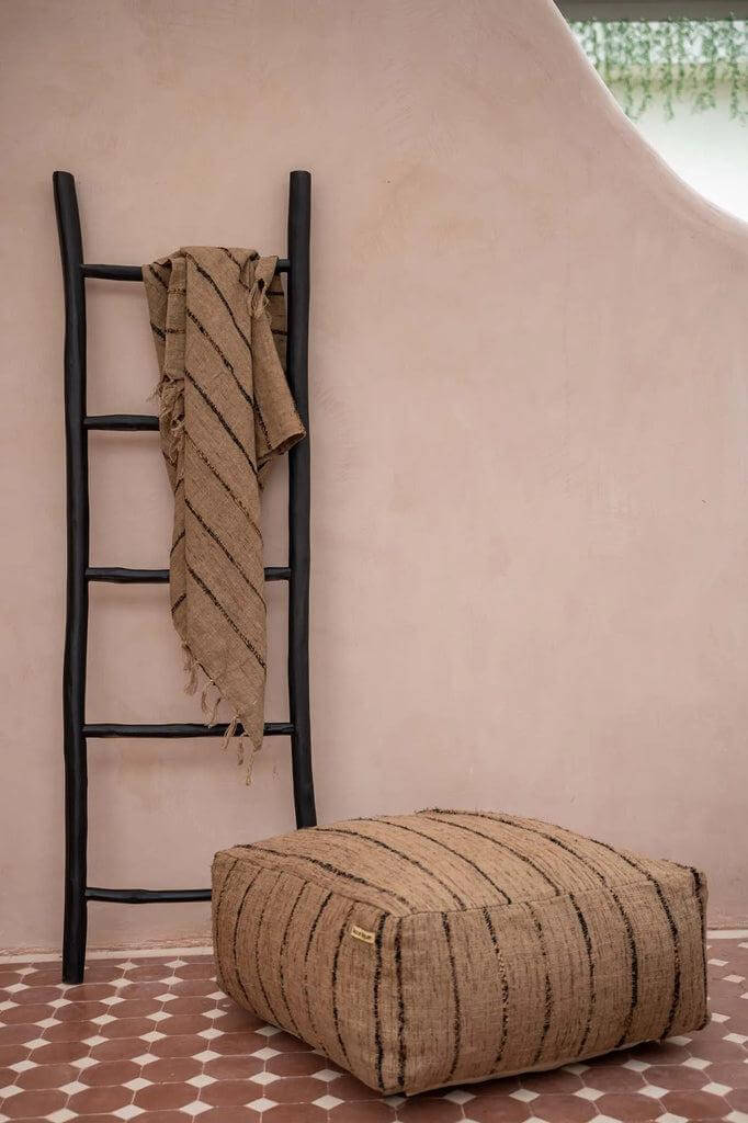 Beige en zwarte katoenen poef met decoratieve trap ernaast, perfect voor huis of gedekte buitenruimte, stijlvol en functioneel.