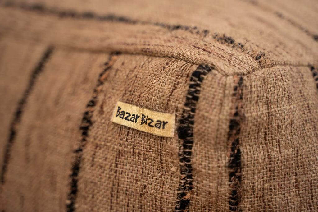 Close-up van katoenen poef met beige en zwarte strepen, voorzien van Bazar Bizar label. Ideaal voor woonkamer en overdekte ruimtes.