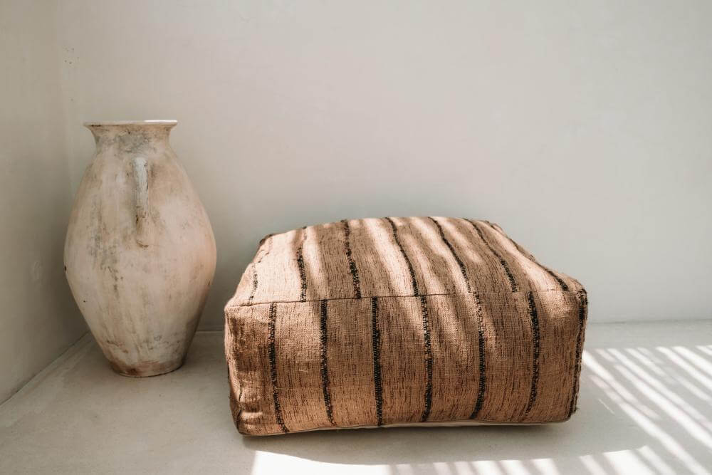 De Oh My Gee Poef in beige en zwart met strepen naast een aardewerken vaas, ideaal voor een stijlvolle zithoek.