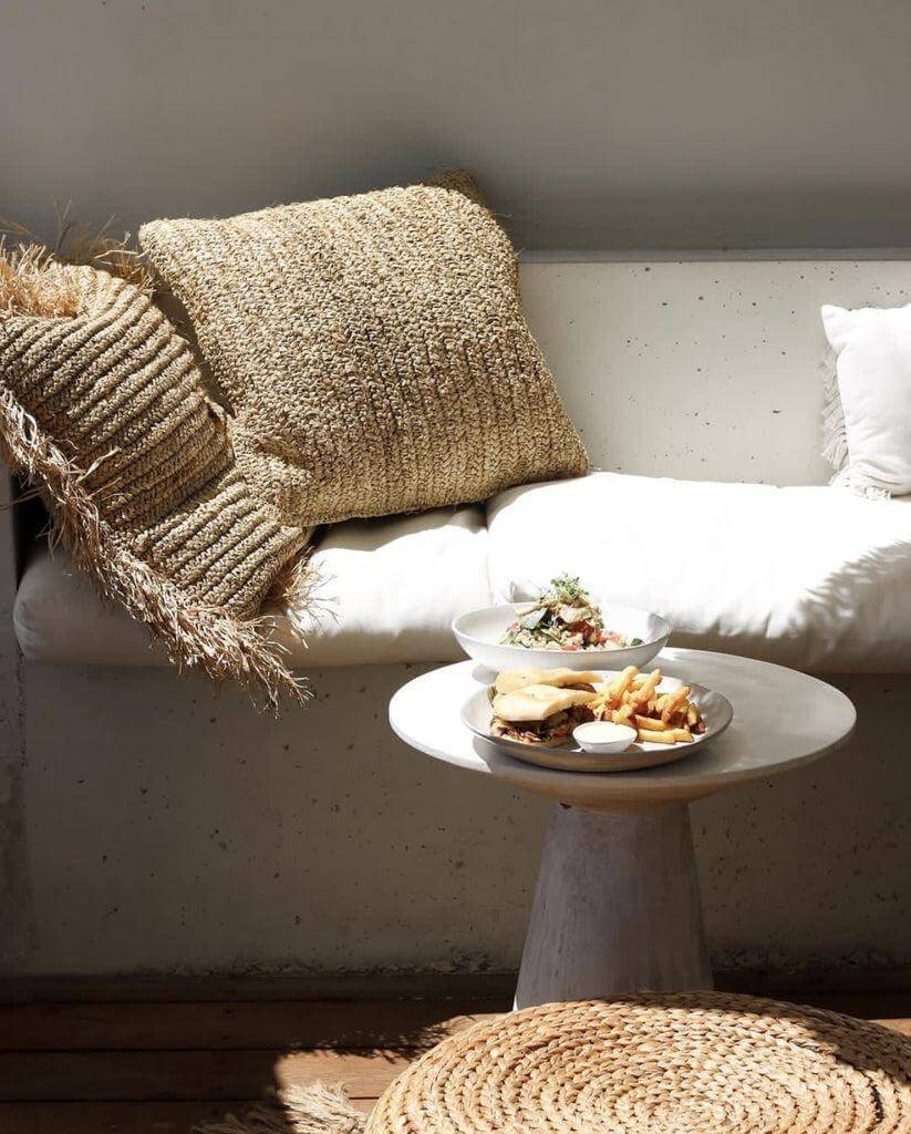 Gezellige zithoek met handgeweven raffia kussenhoes en lichte sofa, perfect voor interieur dat boho en natuurlijke vibes uitstraalt.