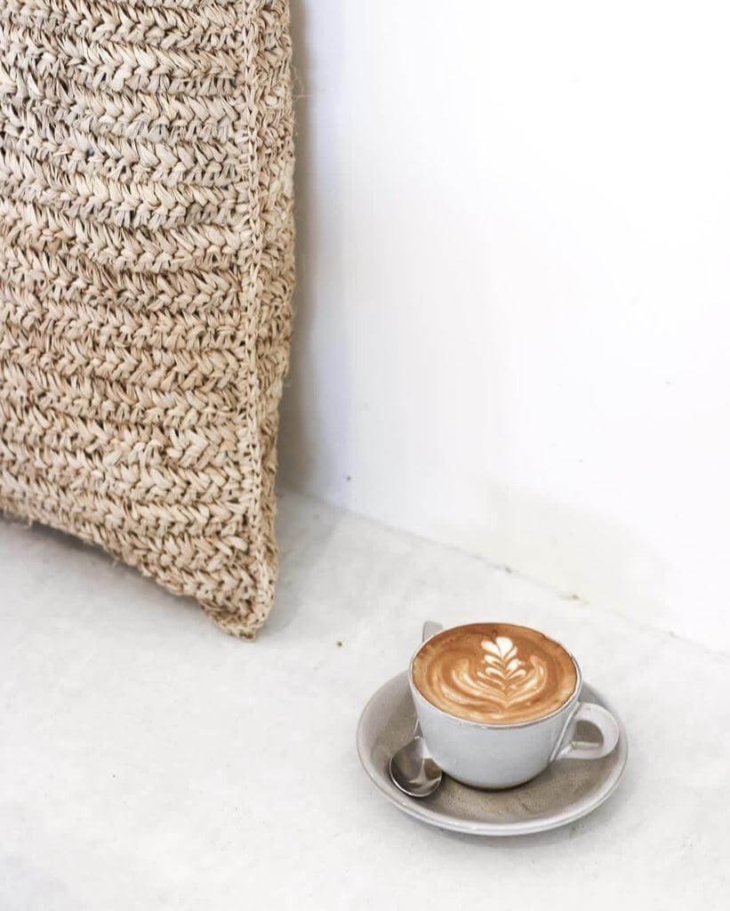 Raffia kussenhoes in naturel tint naast een heerlijke kop koffie, handgemaakt in Indonesië voor een vleugje boho stijl in huis.