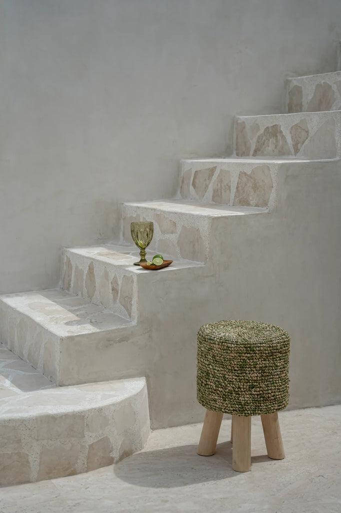 Jungle groene raffia gevlochten kruk naast trap, decoratief en stijlvol interieur accent.