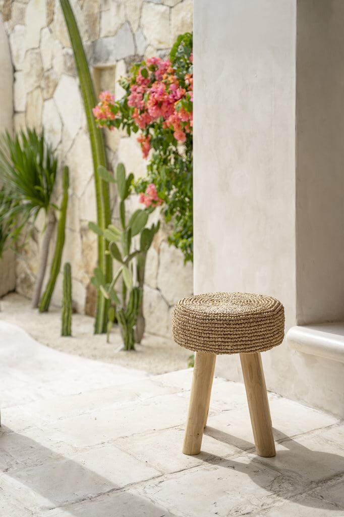 Natuurlijke Raffia Kruk, perfect voor moderne en traditionele interieurs, gefotografeerd in een zonnige tuinomgeving.