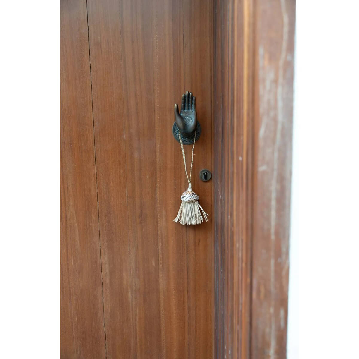 Bohemian-style natural raffia tassel with shells hanging on a decorative hand-shaped wall hook, adding exotic charm to home decor.