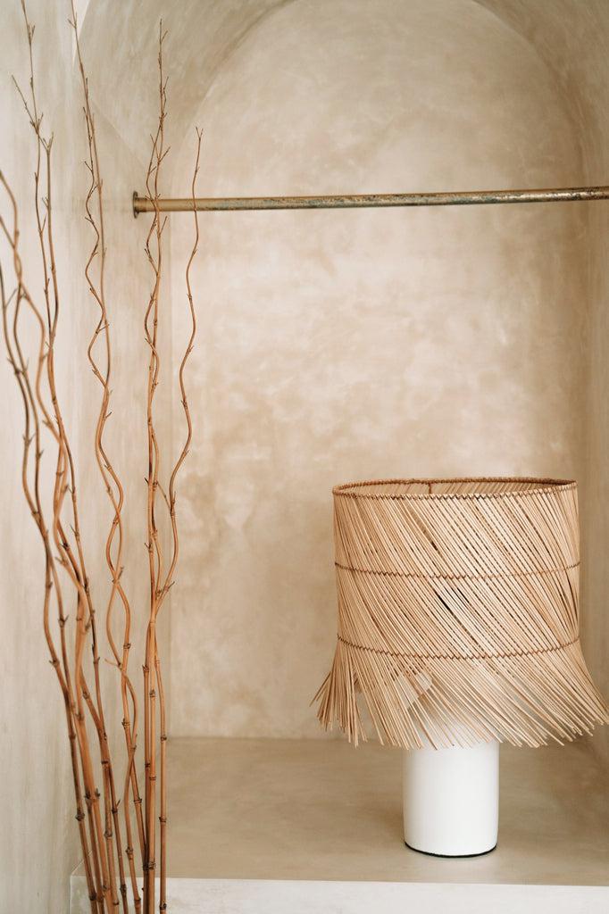 De Rattan Tafellamp - Wit Naturel in een sfeervolle hoek met handgeweven lampenkap van natuurgras. Perfect voor een boho sfeer.