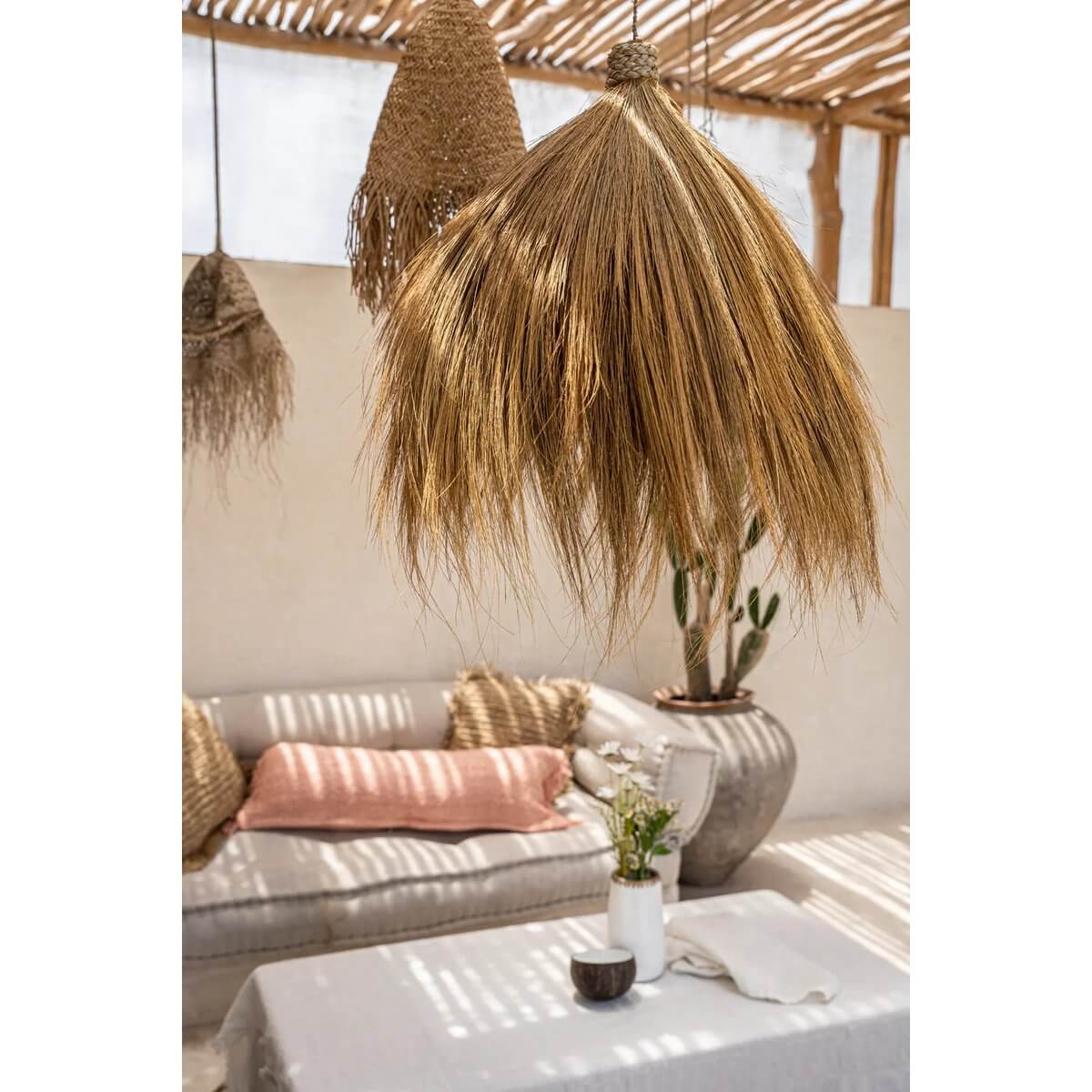 De Rayung Hut-hanger, natuurlijke hanglamp van gras boven een stijlvolle zithoek, creëert warme en uitnodigende gloed voor elk interieur.