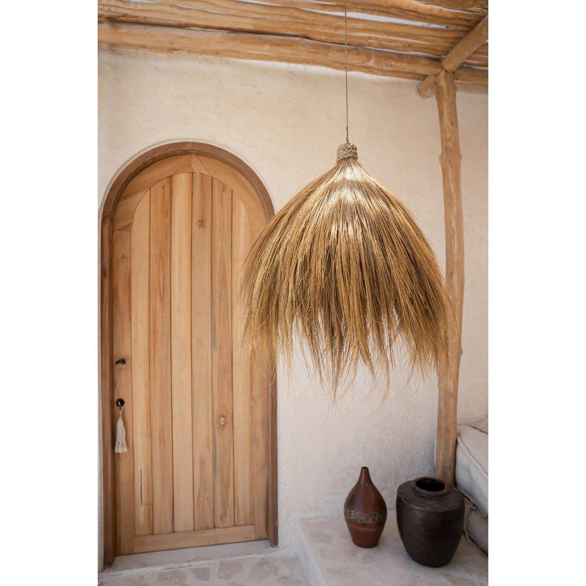 De Rayung Hut-hanger graslamp in een rustieke woonkamer, gezellig en zonnig interieur met natuurlijke houtaccenten.