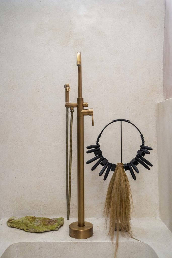 Stijlvol messing kraan naast bohemien decoratie met gras en houten stukken in een moderne badkamer.