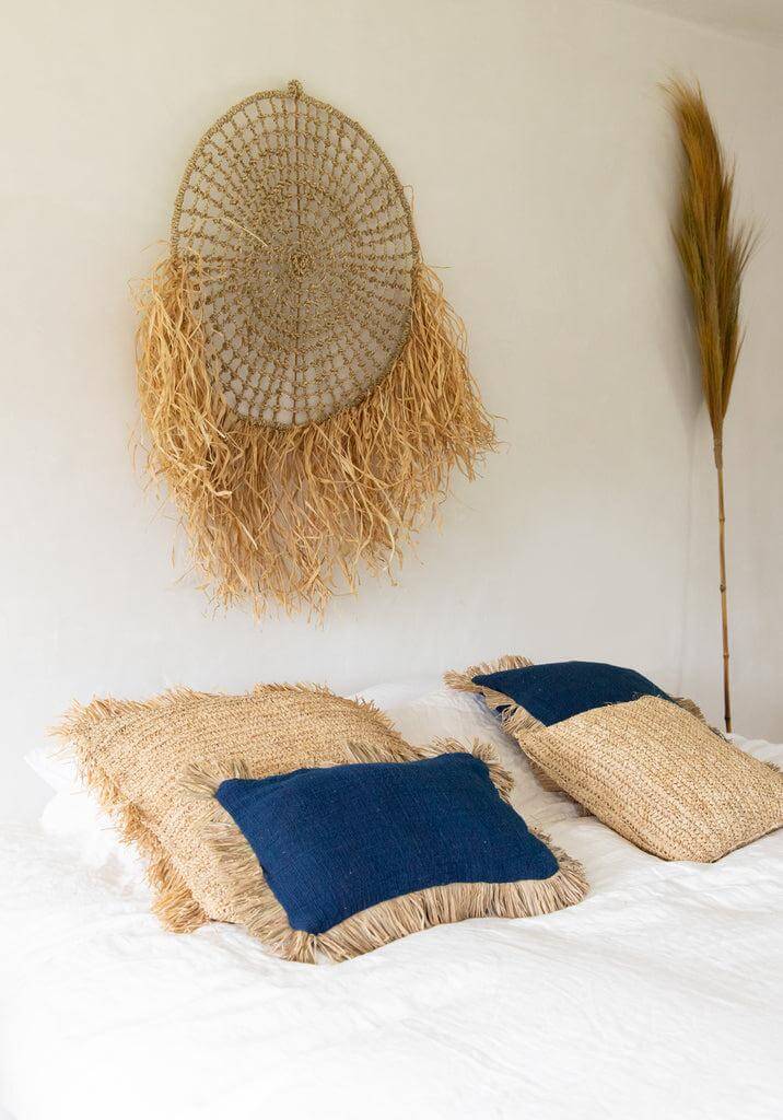 Stijlvolle De Saint Tropez kussenhoes in blauw en naturel op een bed, met sfeervolle raffia franjes, perfect voor een boho interieur.