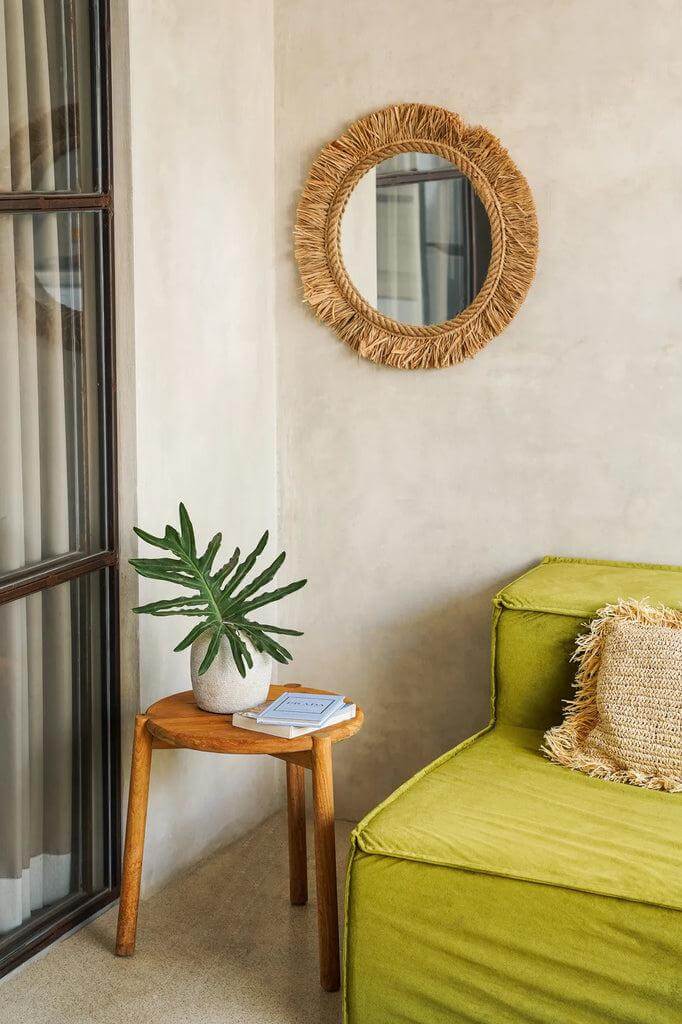 De Seseh bijzettafel van teakhout met plant naast een groene bank in een rustiek interieur, met ronde spiegel aan de muur.
