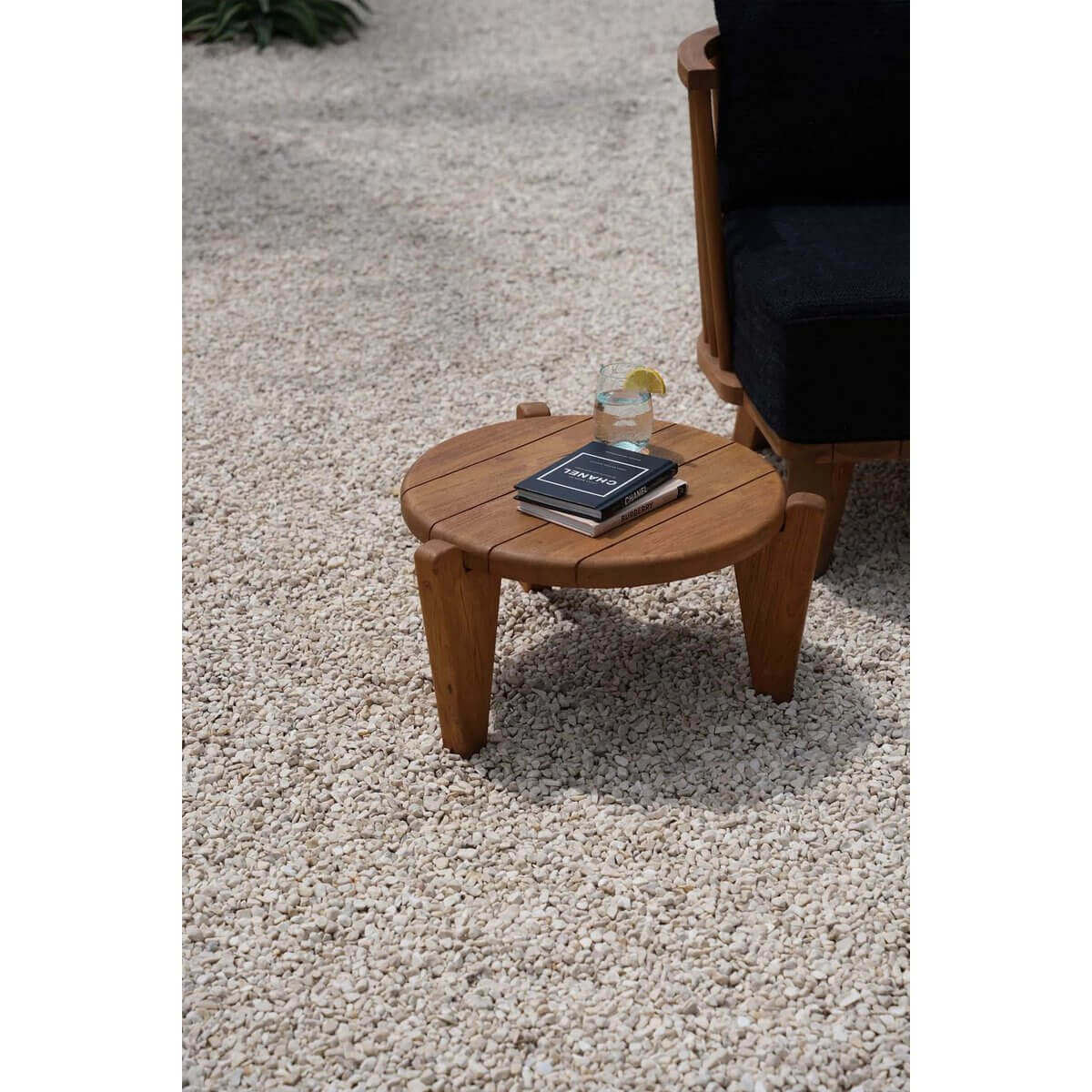 De Seseh salontafel van teakhout op een grindterras met boeken en een glas. Ideaal voor tuin, terras of balkon. Modern en uniek design.