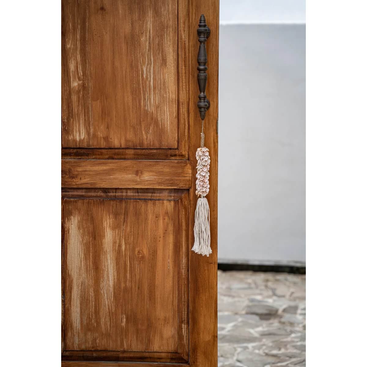 Handcrafted pink shell and cotton hanger on wooden door, bohemian decor, by Balinese artisans. Bazar Bizar Living.