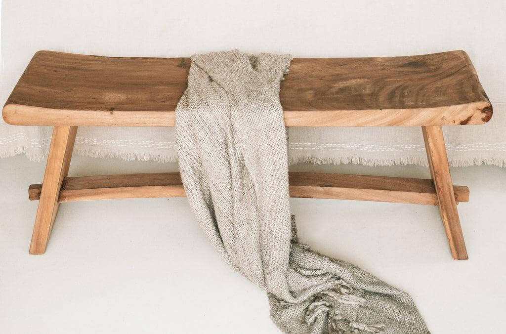 Luxe, beige handgeweven katoenen plaid met franjes op een houten bankje, perfect voor een warme sfeer in huis.