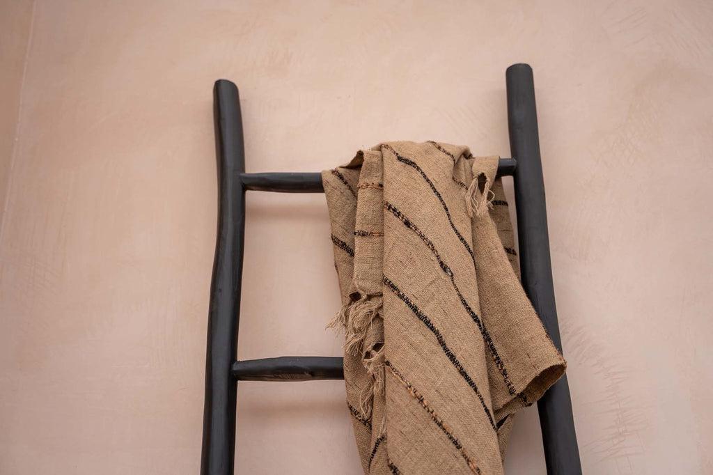 Luxe handgeweven katoenen plaid in beige zwart met franjes op een decoratieve ladder. Gezelligheid voor elk interieur.