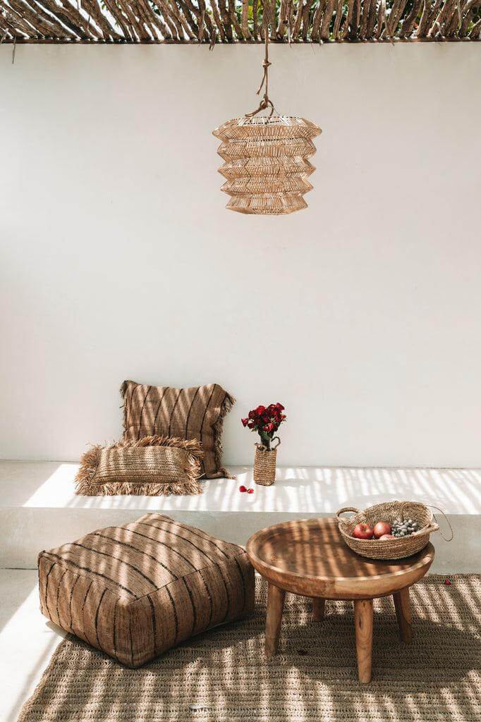 Gezellige zithoek met natuurlijke materialen, inclusief geweven kussen, houten tafel en decoraties onder een beschutte ruimte.