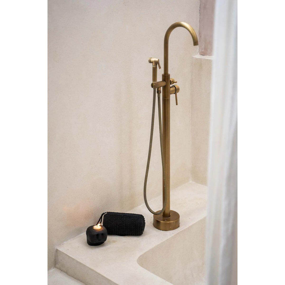 Stijlvolle bronzen douchekraan met zwart kaarsenhouder op beige rand, moderne badkamerafwerking.