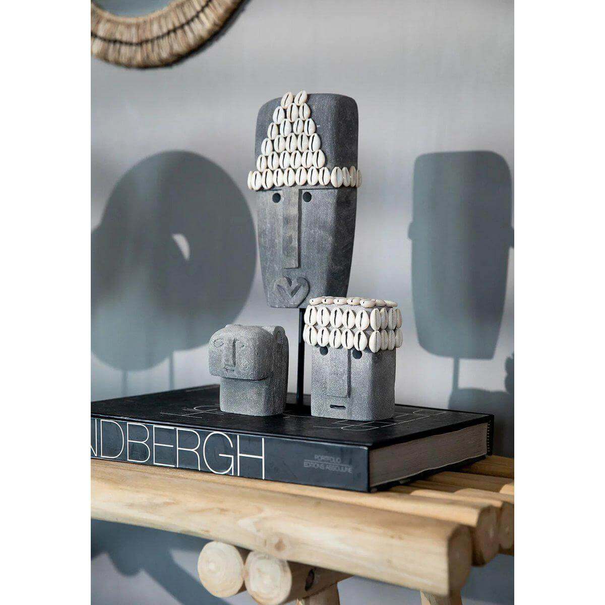 Drie handgemaakte Sumba-stenen beelden op een houten tafel in een interieursetting.