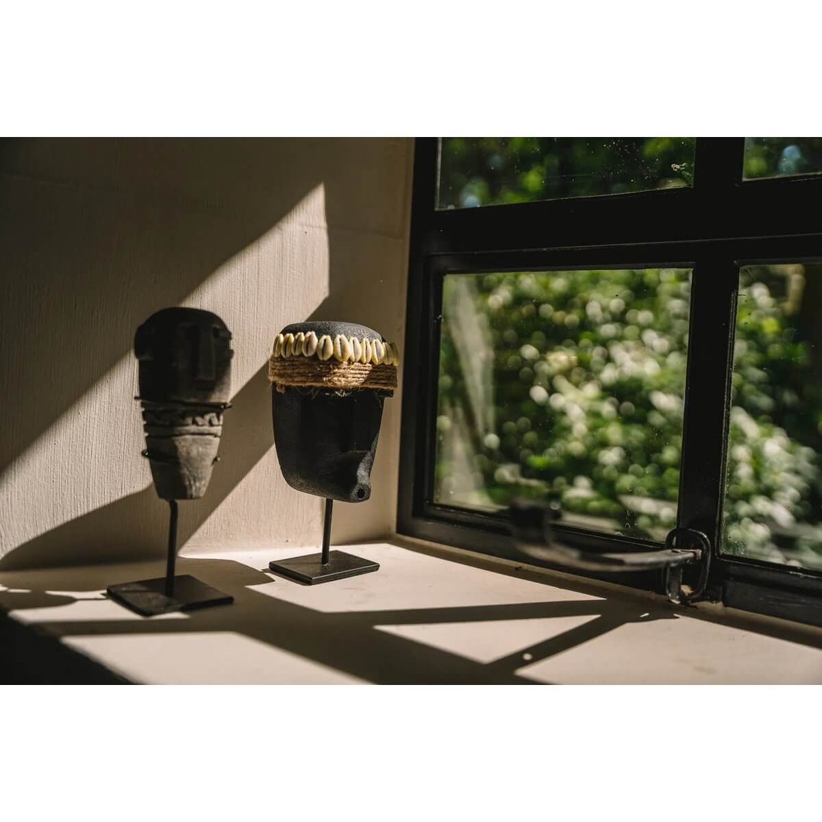 Bohemian Sumba stone figures on stand by a sunlit window, handmade from Indonesian sandstone for protection and healing.