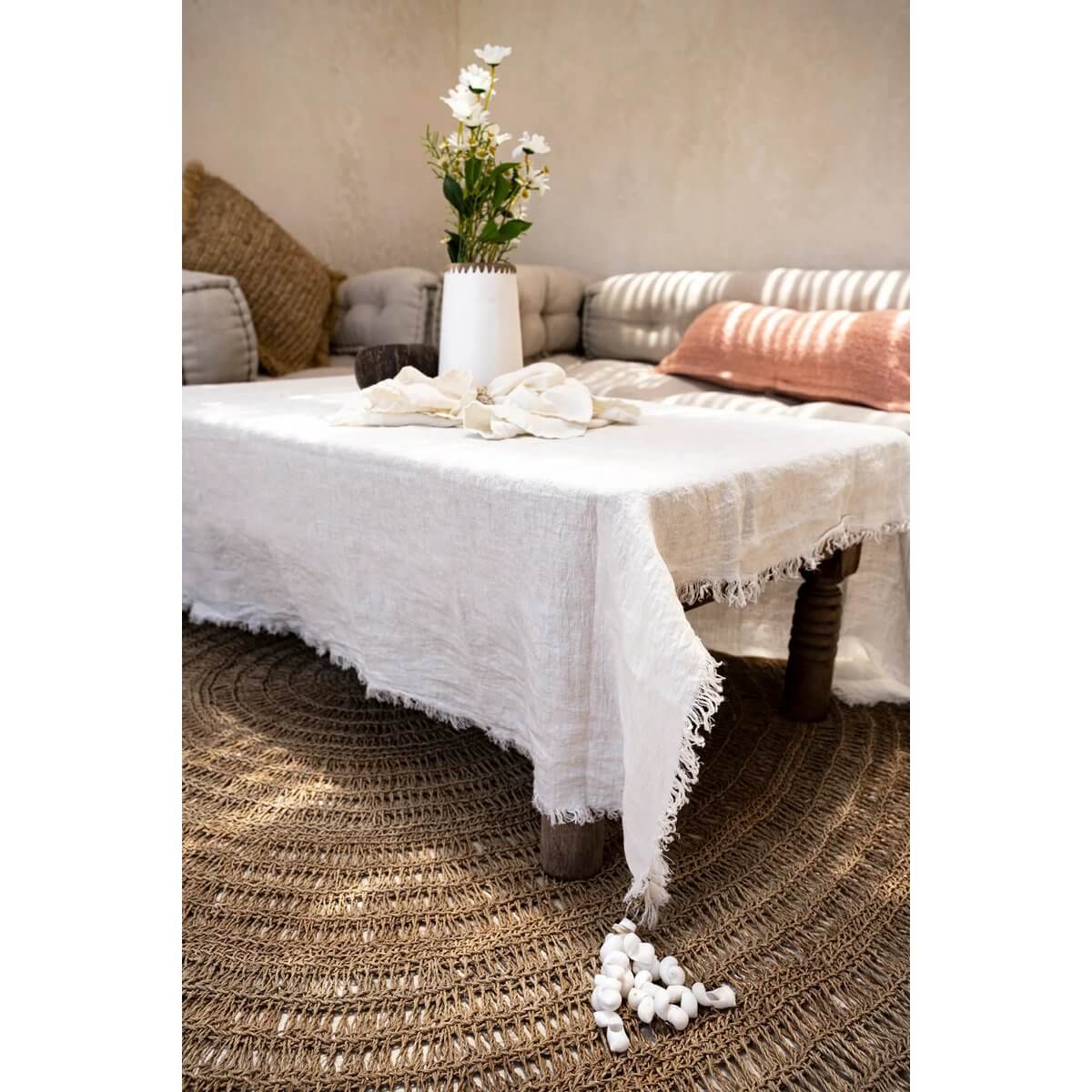 Bohemian table with white cloth and De Tafelkleedhanger set, featuring shell decor in coastal style. Perfect for preventing wind mishaps.