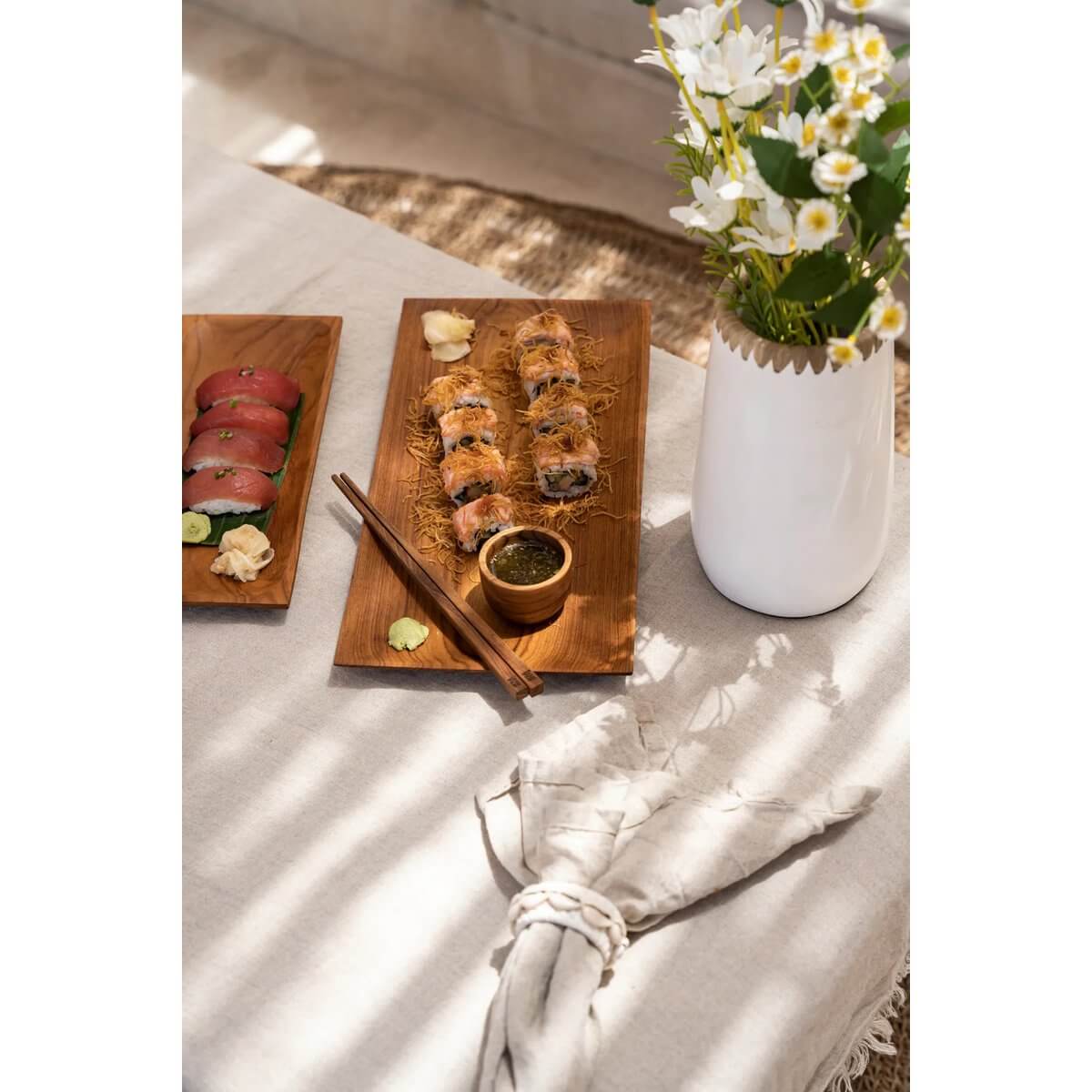 Bohemian dining setup with sushi on wooden platters, a tealight, and flowers in a vase, showcasing natural elegance.
