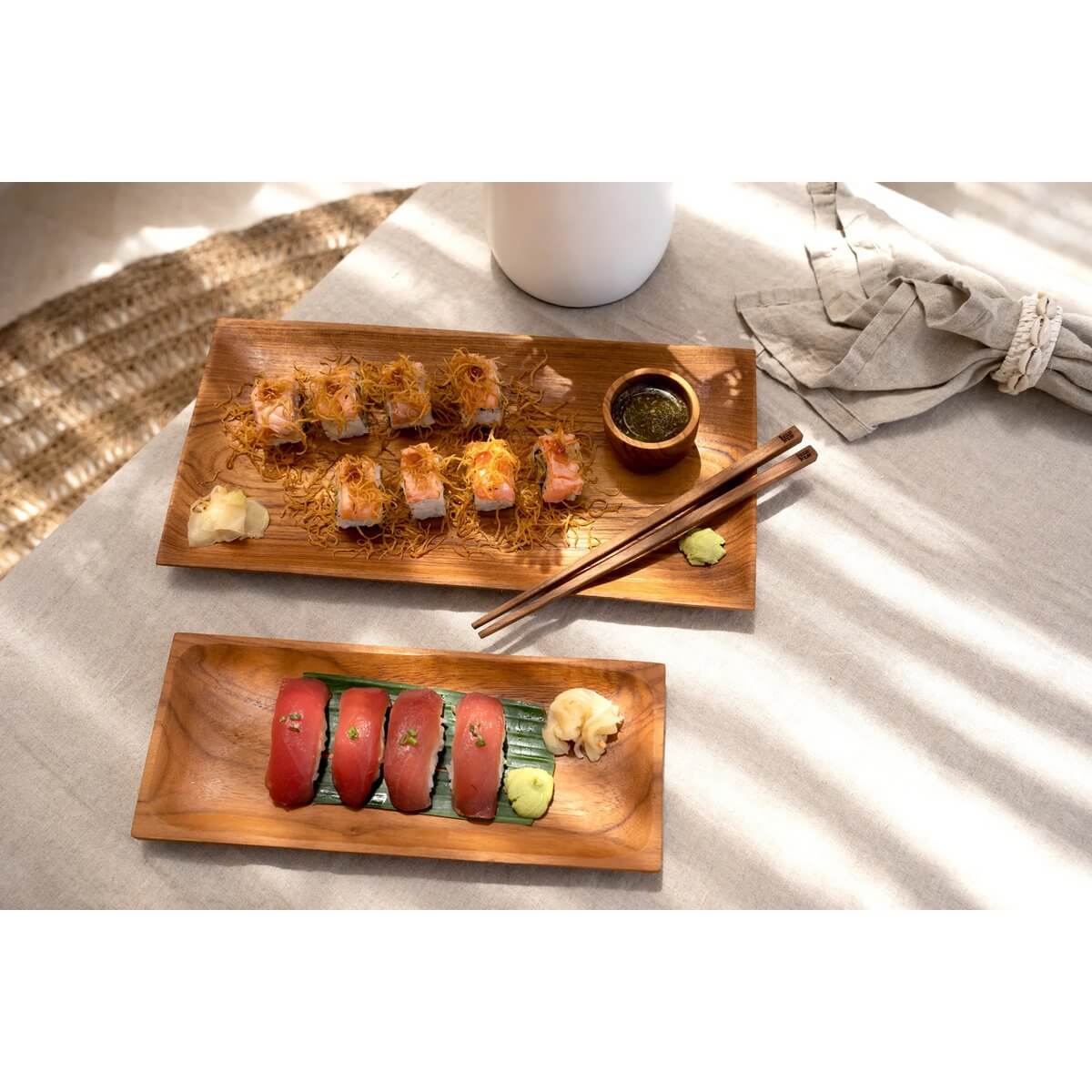 Elegant wooden trays with sushi and condiments on a Bohemian-style table setting, featuring sunlight and a woven table runner.