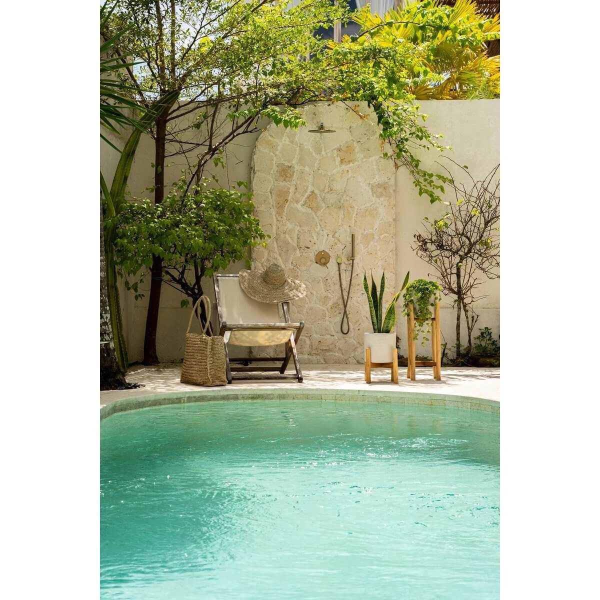 Rustige tuin met zwembad, omgeven door groene planten en een comfortabele stoel met een zomerse tas, perfect voor ontspanning.