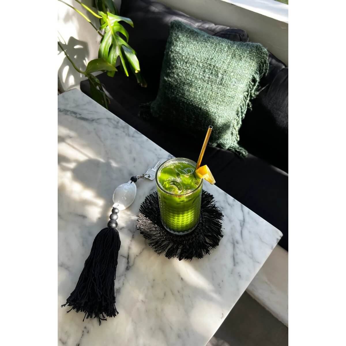 Chic Bohemian black and white Togian keychain with tassel on a marble table, next to an elegant green beverage with a gold straw.
