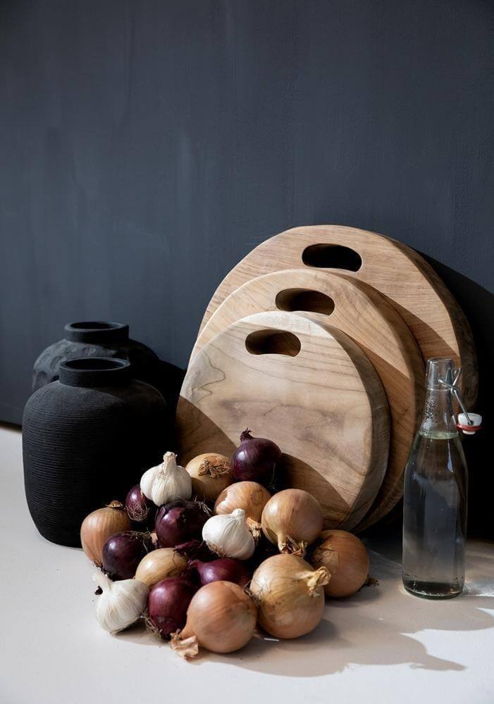 Keukenhoek met zwarte terracotta vazen, houten snijplanken, uien, knoflook en een fles water voor een rustieke uitstraling.