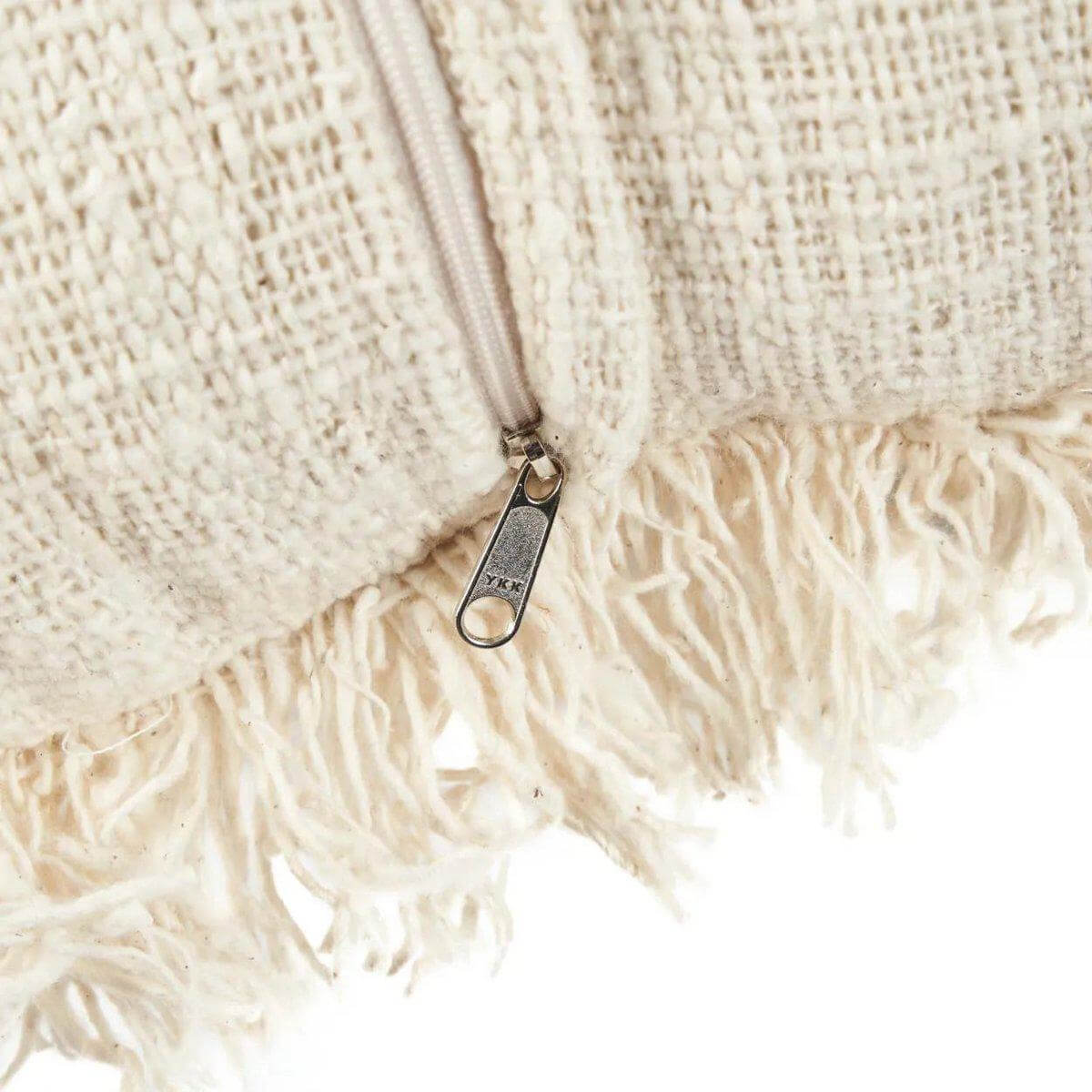 Close-up van een crèmekleurige kussenhoes met ritssluiting en franjes, ideaal voor een boho-stijl interieur.