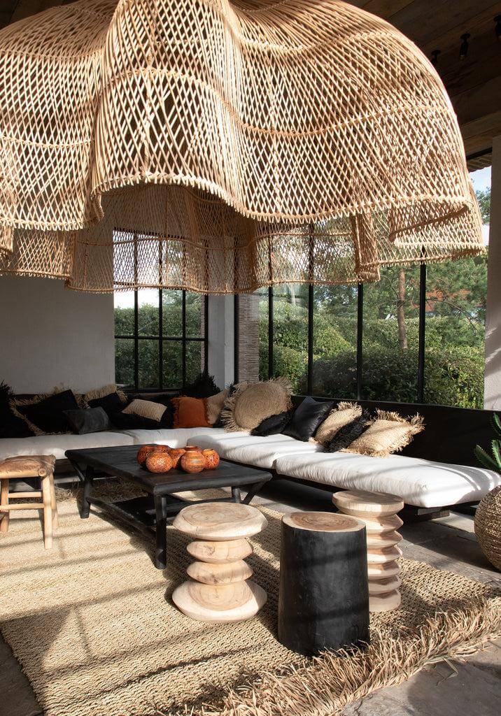 Alt Tag: Gezellige woonkamer met natuurlijke krukken, een zwarte De Tribe Kruk, en een grote gevlochten hanglamp voor een organische sfeer.