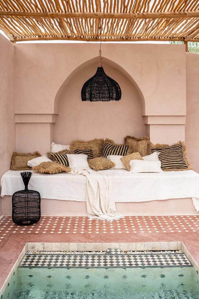 Stijlvolle boho Whipped Hanglamp - zwart, rotan, boven gezellige zithoek met kussens, binnen luxueuze patioomgeving.