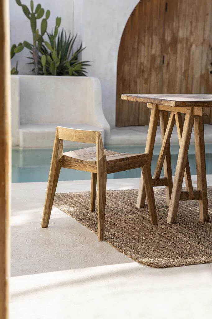 Teakhouten Ydra eetkamerstoel in elegante minimalistische stijl bij houten tafel, geschikt voor binnen en buiten gebruik.