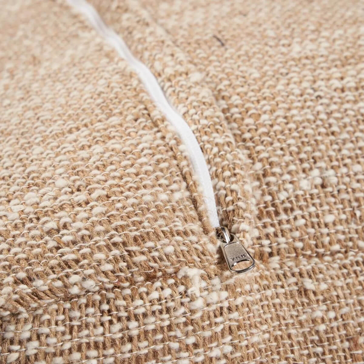 Detail van de beige, zachte stof van de comfortabele poef met stevige rits, ideaal voor stijlvol loungecomfort.
