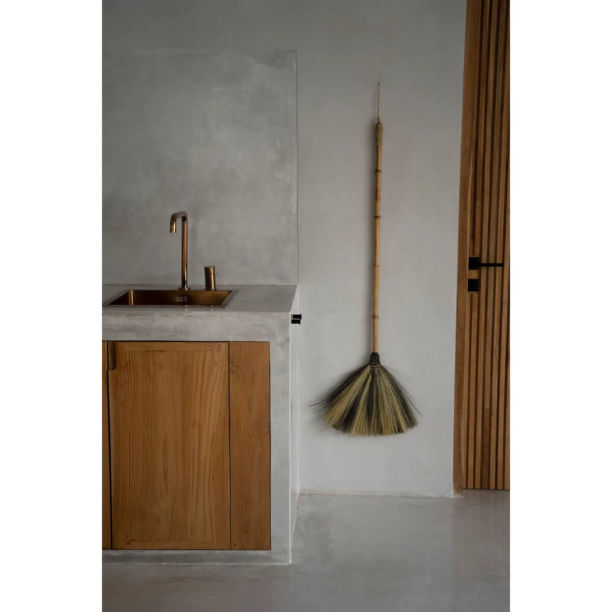 Bohemian style Indonesian broom as decor, featuring natural black grass and wood handle, hanging in a modern interior space.