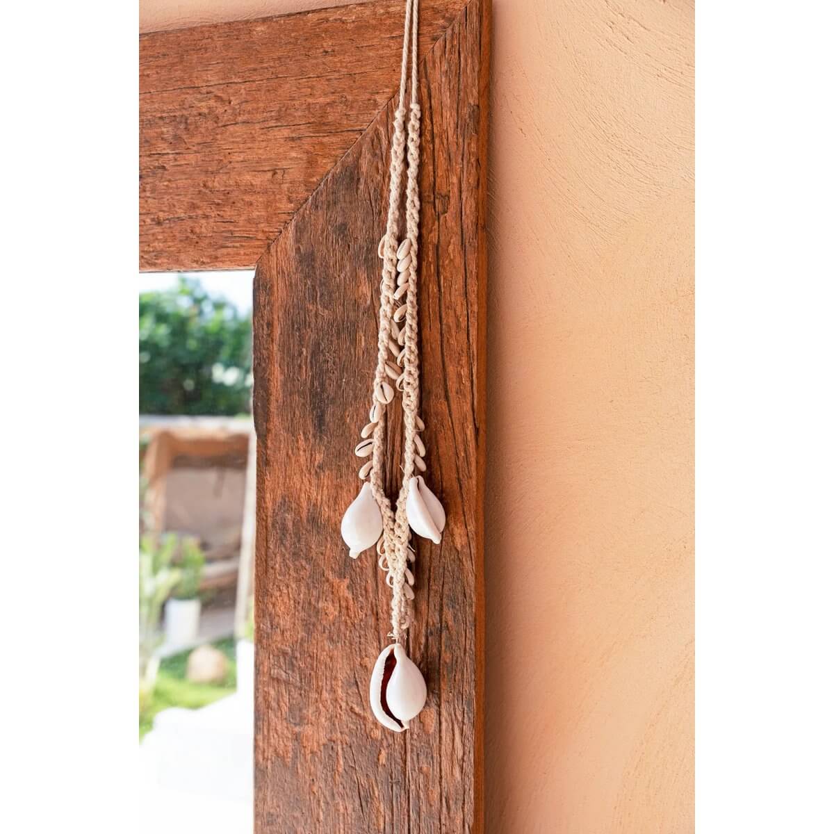 De grote witte kauri schelp ketting aan houten frame voor een vleugje kustflair in huis.