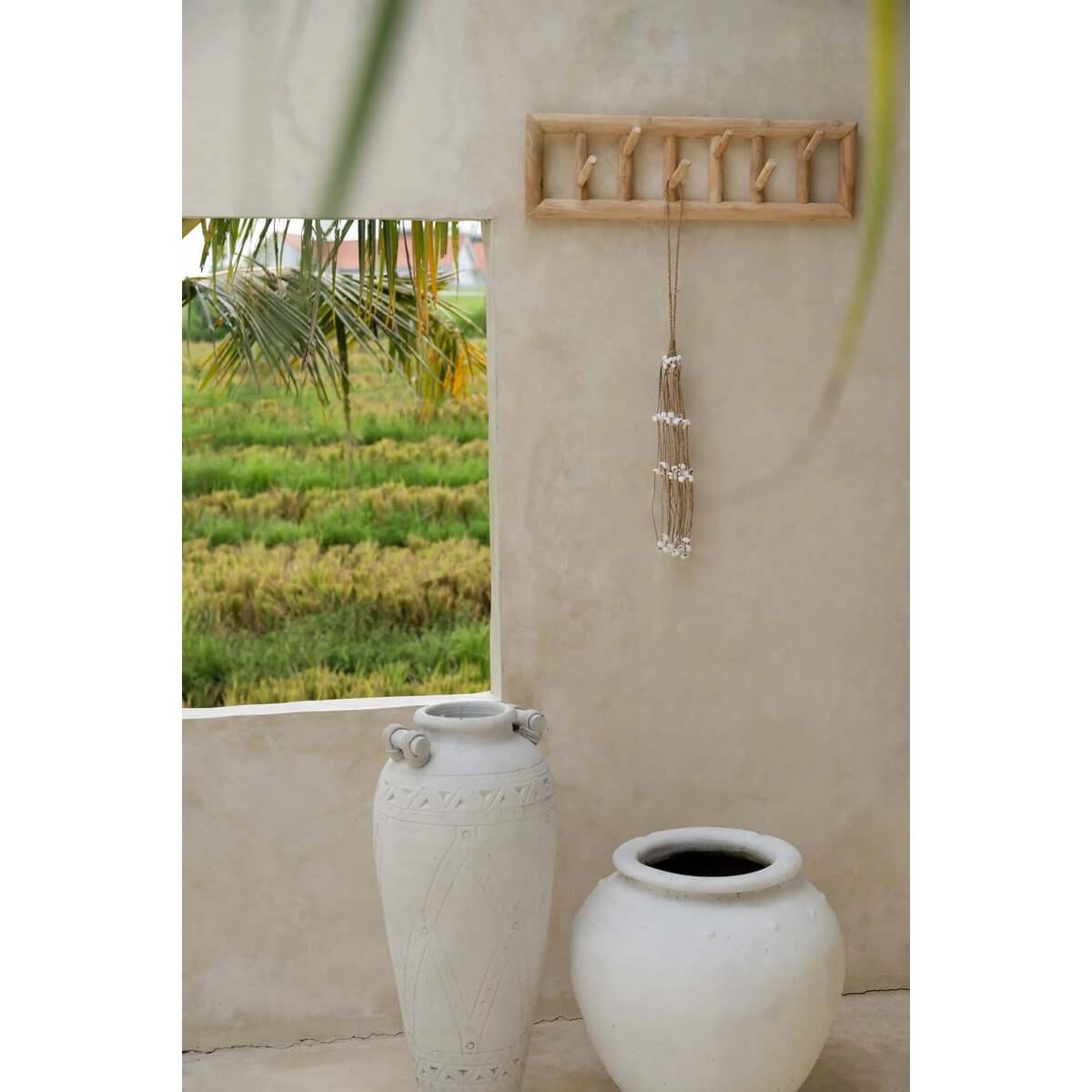 Bohemian shell hanger in white, handmade by Balinese artisans, decorates a wall beside elegant ceramic vases.