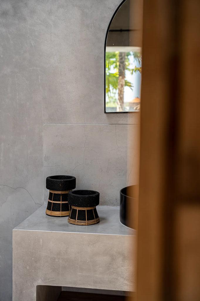 Stijlvolle zwarte terracotta kaarsenhouders met rotanrooster op betonnen tafel in serene kamer