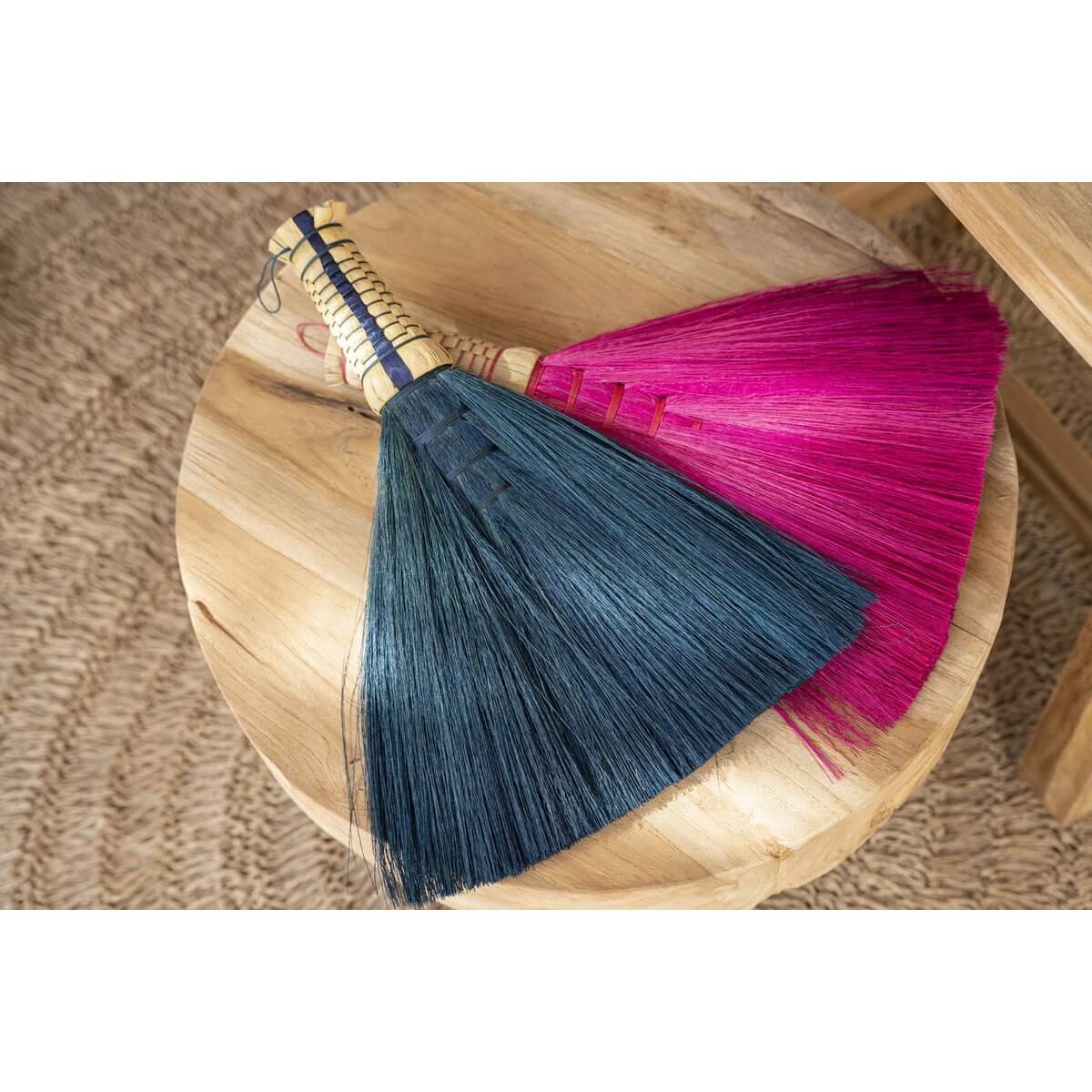 Turquoise and pink Indonesian hand brooms on a wooden surface, perfect for Bohemian decor and effective dust sweeping.