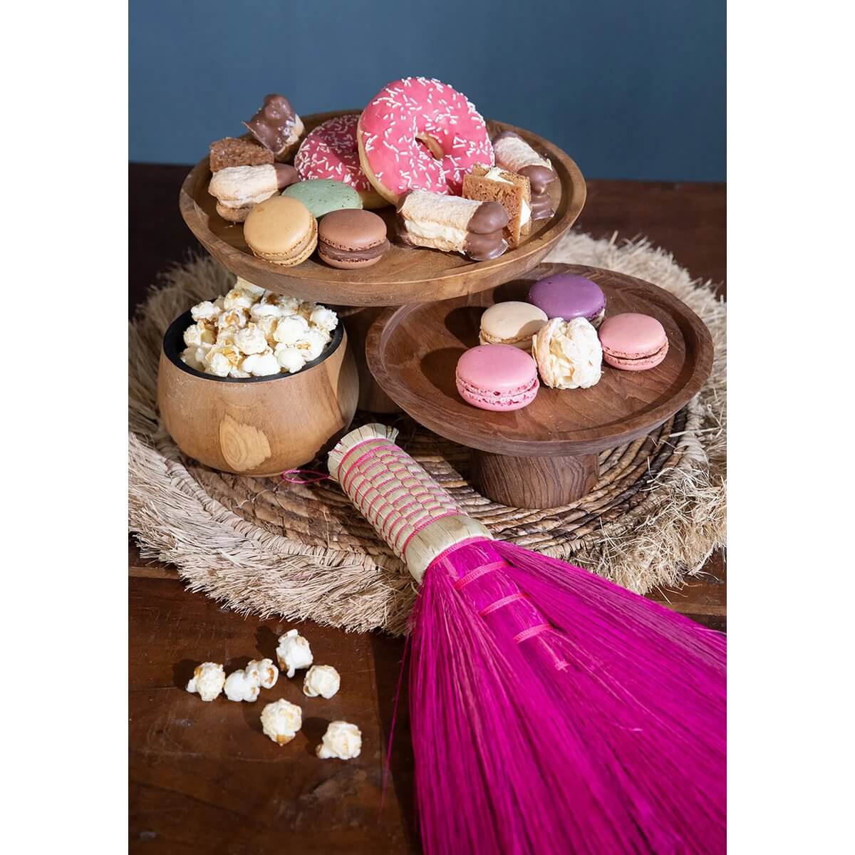 Bohemian pink hand broom with assorted desserts, including macarons and donuts, on wooden stands.