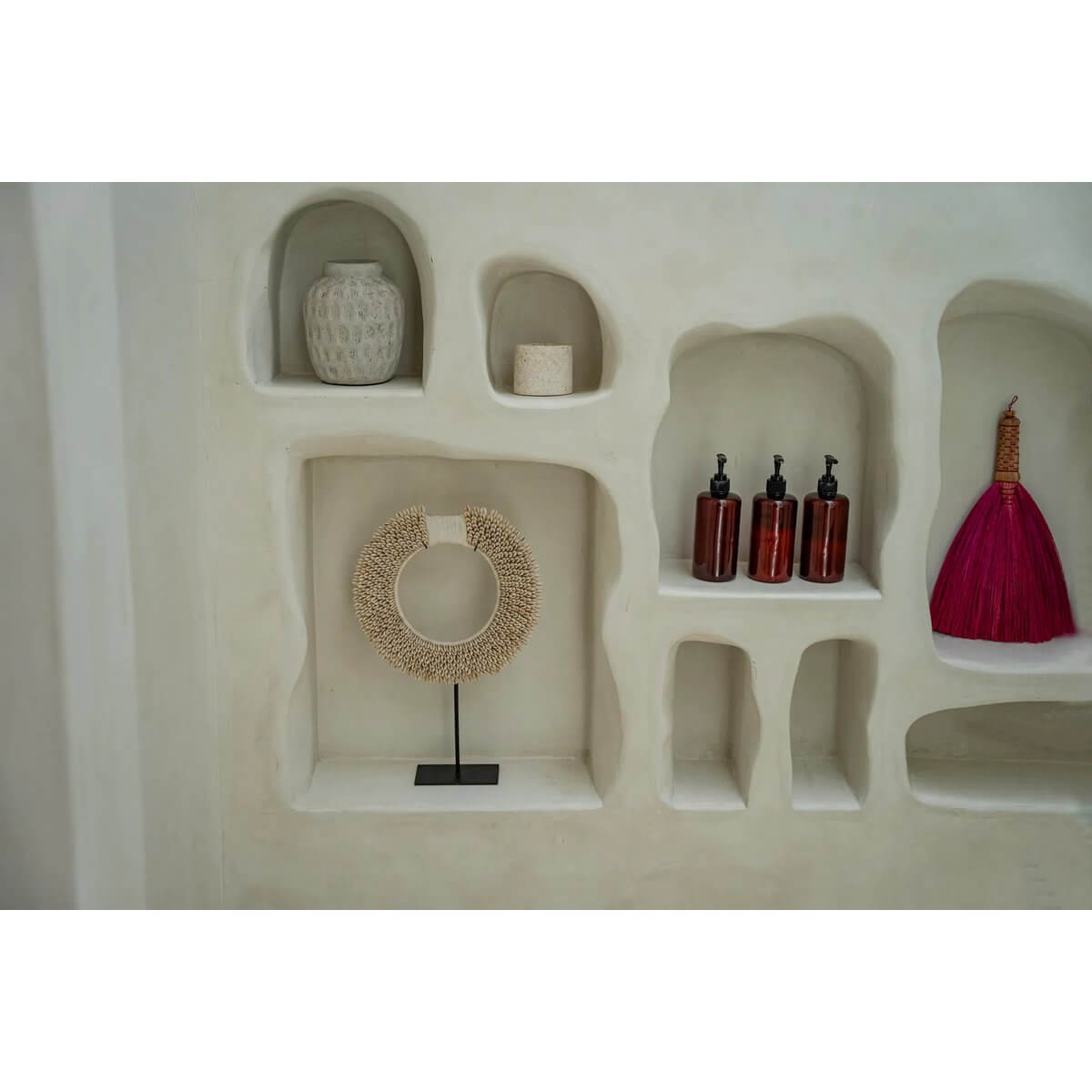 Bohemian decor with Indonesian pink grass hand broom, woven circle piece, and stylish bottles on rustic shelves.