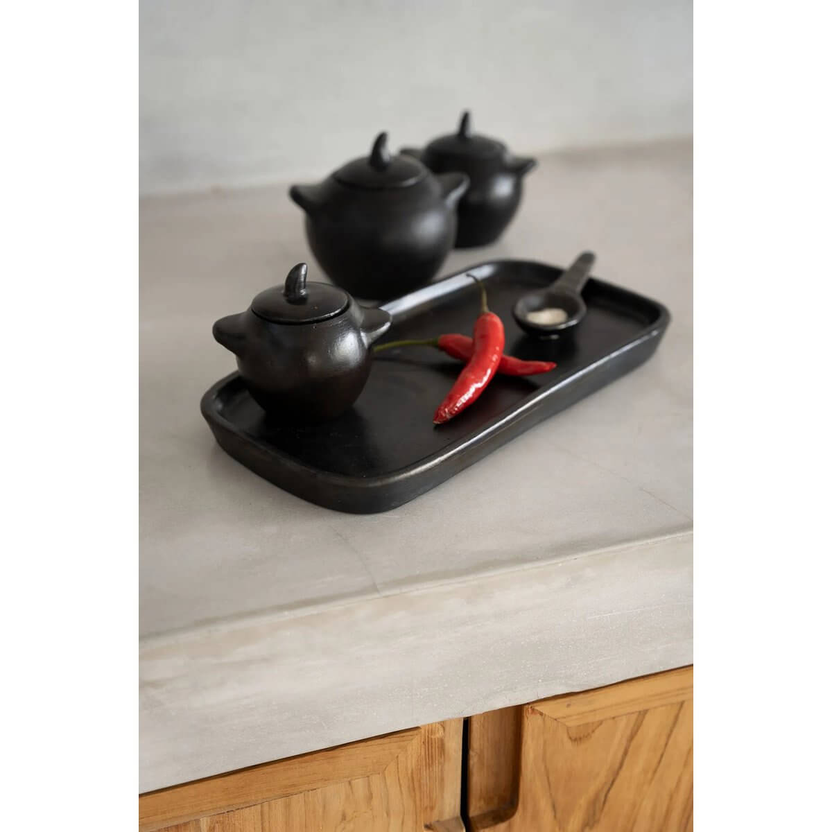 Black-burnt pottery set on tray with chili peppers, perfect for bohemian dining. Enhance your table setting with style and contrast.