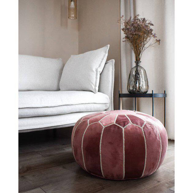 Stijlvolle roze fluwelen poef in een sfeervolle woonkamer met gezellige boho-accenten, perfect als voetenbankje of zitplaats.