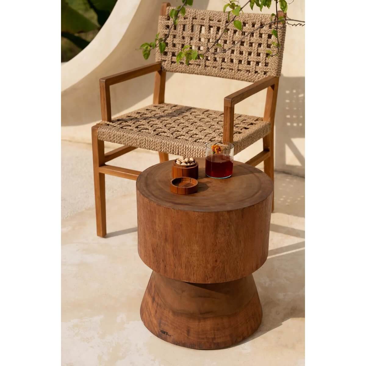 Bohemian outdoor setting with woven chair and wooden table featuring Het On the Rocks-glas and a refreshing drink.