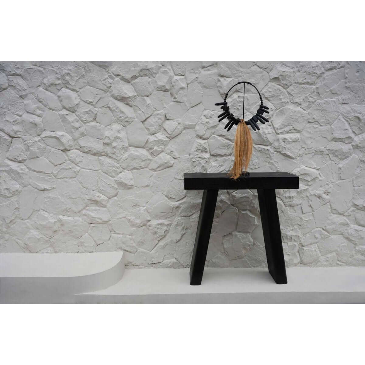 Stijlvolle Rayung-hout display op zwarte standaard, een bohemian decorstuk met twee houten poten tegen witte stenen muur.