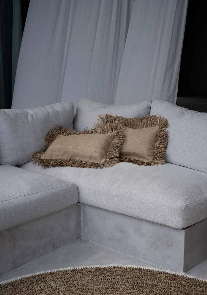 Witte hoekbank met beige kussens en rond zeegras vloerkleed in een moderne woonkamer.