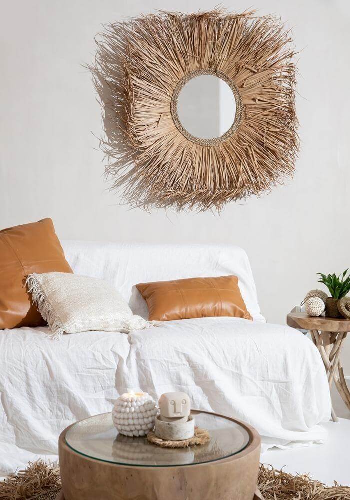 Stijlvolle woonkamer met lederen kussenhoezen en rieten decor, omgeven door natuurlijke elementen en een spiegel met rieten omlijsting.