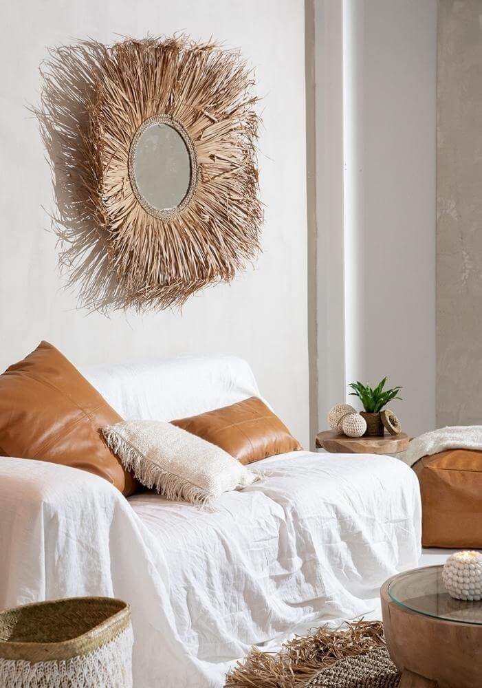 Stijlvolle woonkamer met leren Six Panel kussen, wit laken en decoratieve wandspiegel, natuurlijke en elegante setting.